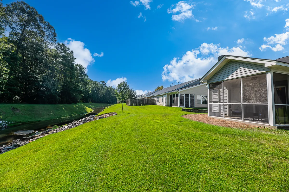 The lush green lawn and meandering stream in front of the building create a tranquil outdoor setting. The space is perfect for morning coffee or evening strolls, tying into the lifestyle of both exploration and relaxation.