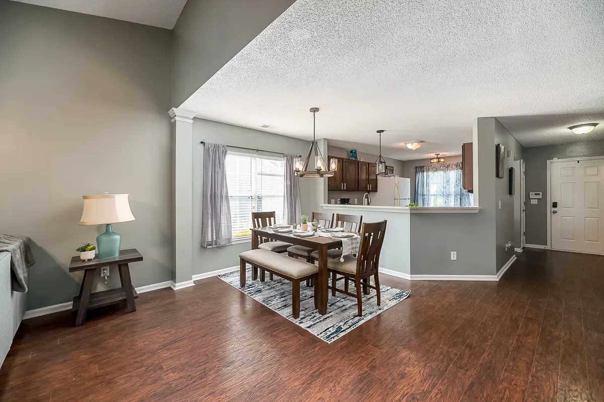 A warm, inviting dining table is set in the foreground, with a view into the adjacent kitchen and a cozy sofa nearby. The scene evokes family dinners and casual gatherings, emphasizing the flow of space and shared experiences.