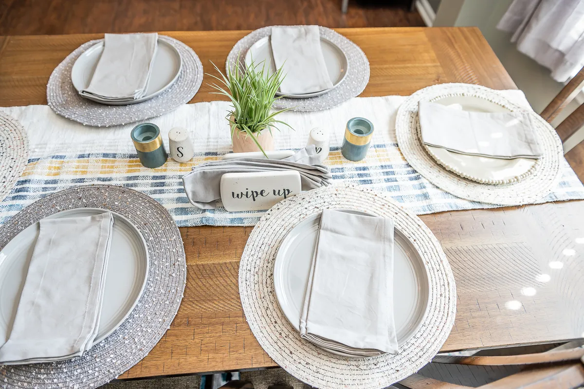An inviting dining table set with plates, napkins, a centerpiece plant, and a textured table runner, ready for gatherings or celebratory meals. The overall mood is bright and welcoming, promoting togetherness.