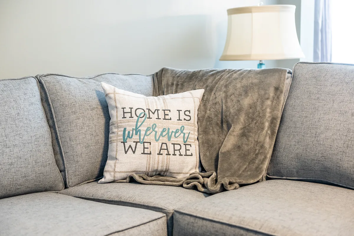 A sectional couch adorned with soft throw blankets and decorative pillows, accompanied by a cozy lamp, all suggesting a welcoming atmosphere ideal for relaxing, reading, or gathering with loved ones.